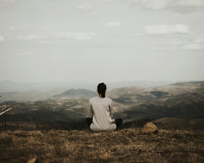 Photo by Milan Popovic woman sitting on cliff overlooking mountains during daytime